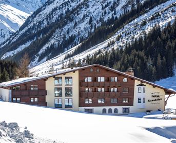 Ein stilvolles Hotel inmitten einer verschneiten Berglandschaft. Die Umgebung ist geprägt von hohen Tannen und majestätischen Bergen.