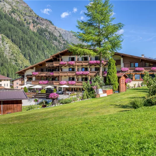 Ein charmantes Hotel in den Bergen mit bunten Blumen auf den Balkonen. Der grüne Rasen und die beeindruckende Landschaft laden zum Entspannen ein.
