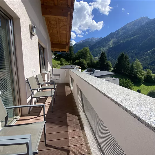 A balcony with several chairs and a beautiful view of the mountains. The sky is blue and partially cloudy.
