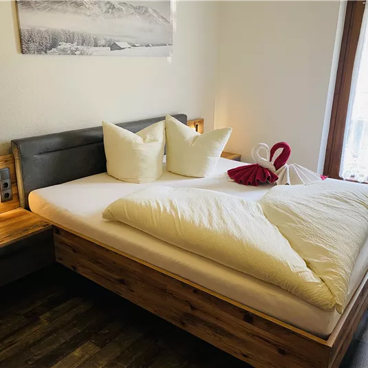 A cozy bedroom with a large bed and decorative pillows. The wooden details and the windows give the room inviting warmth.