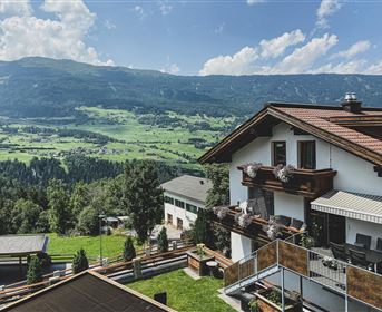 A picturesque view of green meadows and mountains. In the foreground, there is a cozy house with a balcony.