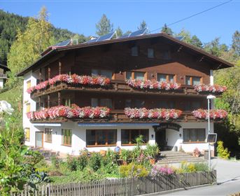 Ein charmantes Holzhaus mit einem blühenden Balkon und einem gepflegten Garten. Umgeben von Bäumen und einer schönen Landschaft.
