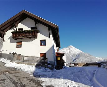 A winter house in the snow with a clear blue sky. Snow-covered mountains are visible in the background.