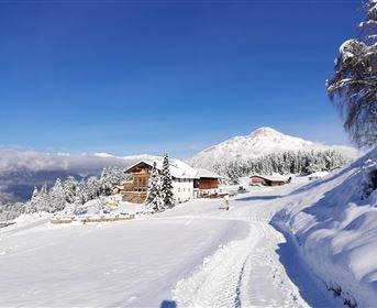 Eine schneebedeckte Landschaft mit traditionellen Hütten und einem klaren blauen Himmel. Im Hintergrund sind schneebedeckte Berge zu sehen.