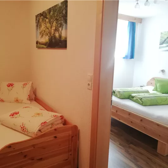 A cozy bedroom with two wooden beds. There are green cushions and pictures on the walls that create a pleasant atmosphere.