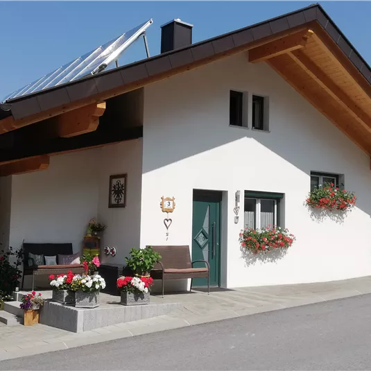 Ein charmantes Haus mit einem modernen Dach und schönen Blumenarrangements an der Fassade. Der Eingang ist freundlich gestaltet und von einer ruhigen Umgebung umgeben.