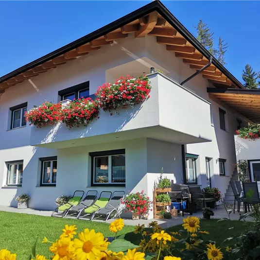 Ein modernes Haus mit einem Garten, in dem bunte Blumen blühen. Die Fenster sind mit Blumenkästen dekoriert und es gibt gemütliche Liegestühle auf der Terrasse.