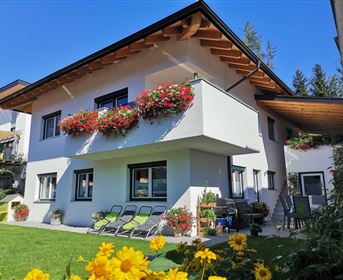 Ein modernes Haus mit einem Garten, in dem bunte Blumen blühen. Die Fenster sind mit Blumenkästen dekoriert und es gibt gemütliche Liegestühle auf der Terrasse.