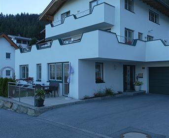 A modern house with a balcony and a well-maintained garden landscape. The surroundings are surrounded by mountains and the sky is clear.
