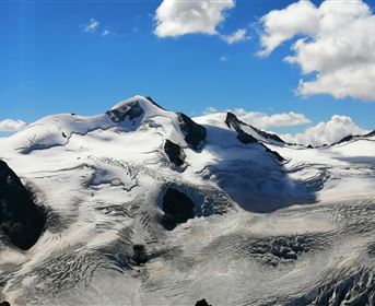 Ein beeindruckendes Bergpanorama mit schneebedeckten Gipfeln und einem klaren blauen Himmel. Die Gletscherflächen glänzen in der Sonne.