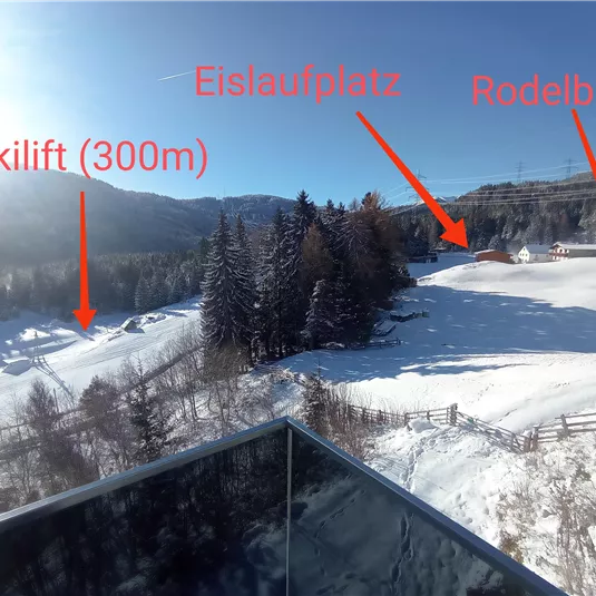 A winter landscape with a ski lift nearby and a toboggan run. The surroundings are characterized by snow-covered trees and hills.