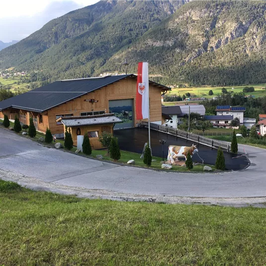 Ein modernes Holzgebäude in einer bergigen Landschaft. Die österreichische Flagge weht vor dem Gebäude.