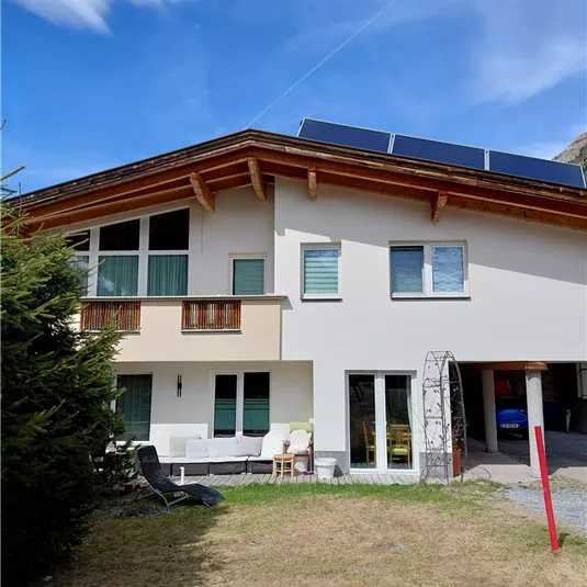 A modern house with a balcony and solar panels on the roof. The garden is green and inviting, perfect for relaxed hours outdoors.