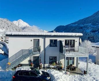Ein modernes Haus im Schnee mit einem klaren blauen Himmel. Im Vordergrund steht ein schwarzes Auto und die Umgebung ist winterlich bedeckt.