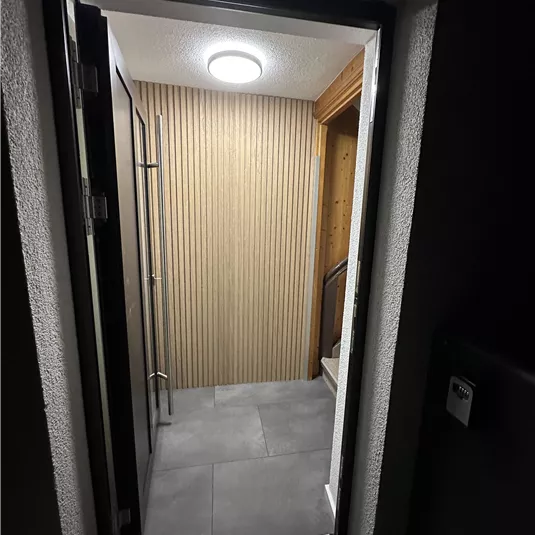 A bright entrance door with decorative walls. The floor is modern tiled and there is a staircase in the background.