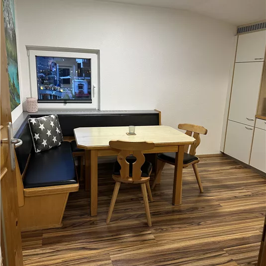 A cozy dining area with a table and chairs. A windowsill overlooking the outside and a warm wooden floor give the room an inviting atmosphere.