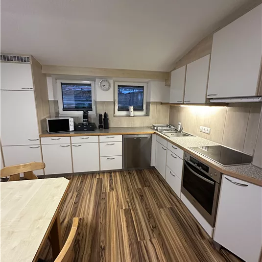 A modern kitchen with white cabinets and hardwood floors. It is well equipped with a stove, sink, and refrigerator.