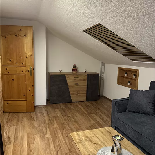 A cozy attic room with a modern couch and a wooden table. 

Against the wall is a sideboard and the floors are made of wood.
