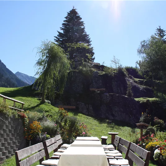 An invitingly set table in a picturesque mountain landscape. In the background, tall trees and a clear view of the sky can be seen.