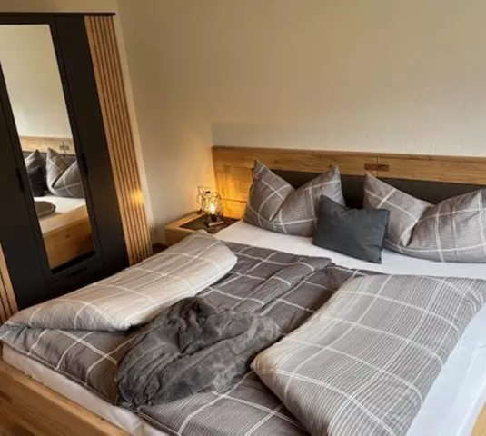 Ein modernes Schlafzimmer mit einem Doppelbett und eleganten Kissen. Ein großer Schrank steht neben dem Bett, und der Raum ist hell und einladend.