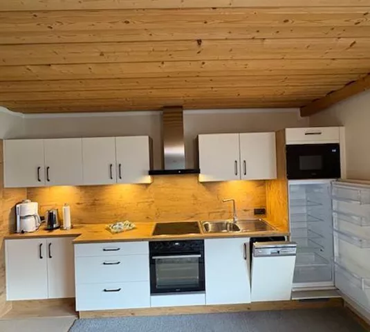 Eine moderne Küche mit weißen Schränken und Holzdetails. Sie ist ausgestattet mit Herd, Geschirrspüler und Kühlschrank.