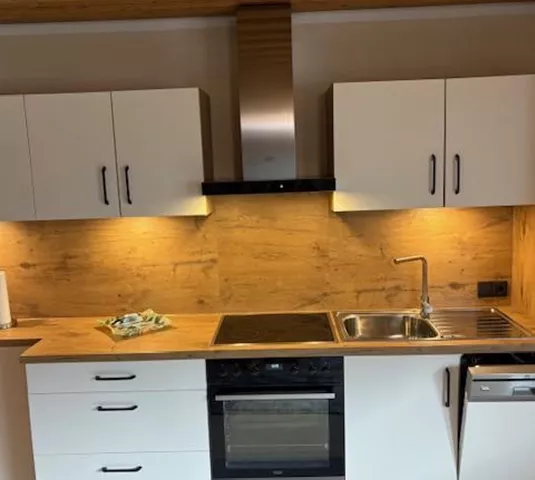 Eine moderne Küche mit weißen Schränken und Holzverkleidung. Der Raum ist gut beleuchtet und zeigt einen Herd, eine Spüle und eine Spülmaschine.