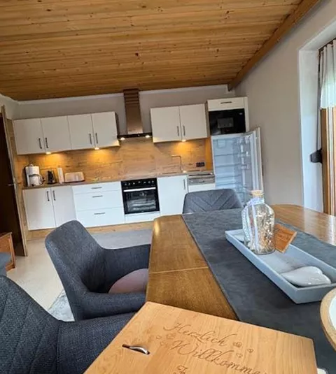 Eine moderne Küche mit einem Holztisch und gemütlichen Stühlen. Die Wände sind hell und die Decke ist aus Holz, was eine warme Atmosphäre schafft.