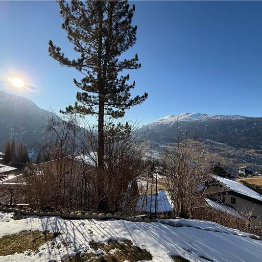 A picturesque mountain landscape with snow-covered roofs and gentle hills. The sun shines over the mountains, creating a clear, calm atmosphere.