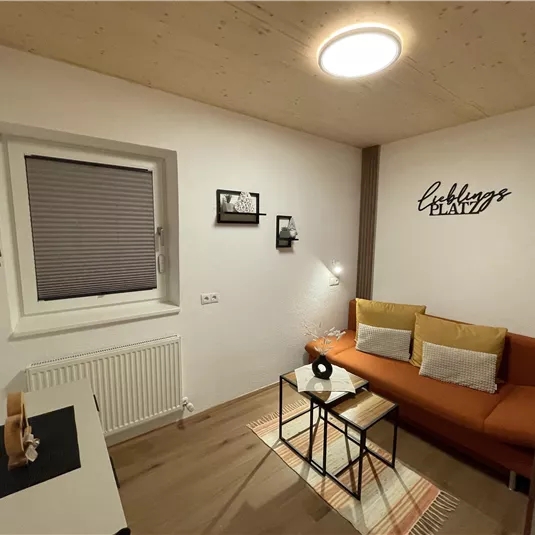 A cozy living room with an orange sofa and a small table. The walls are light and there is a television as well as decorative picture frames.