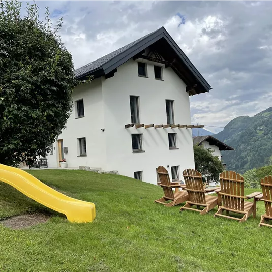 A beautiful house with a lawn and a slide. In the foreground, there are comfortable chairs overlooking the mountains.