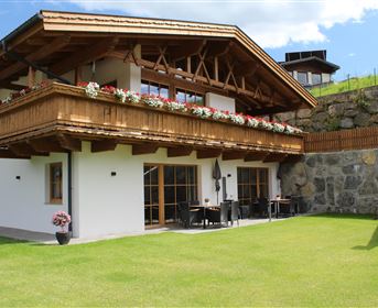 Ein gemütliches Holzhaus mit einem Balkon voller Blumen. Der Garten ist grün und einladend.
