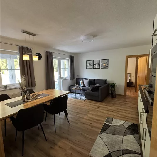 A modern living room with a gray sofa and a dining table. Bright colors and wooden floors create an inviting atmosphere.