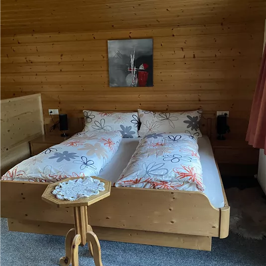 A cozy bedroom with a double bed and colorful bedding. The walls are made of wood and there is a small table next to the bed.