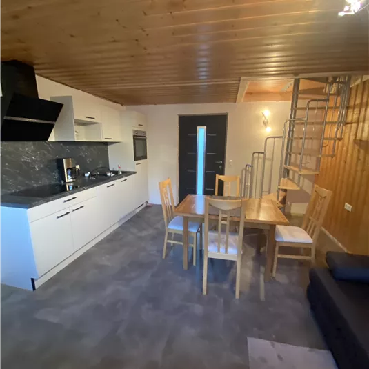 A modern kitchen with a dining area and wooden ceiling. The staircase leads to an upper floor.