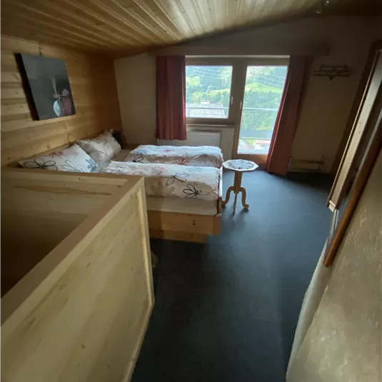 A cozy room with a wooden ceiling and two beds. Large windows let in plenty of light and offer a view of the greenery.