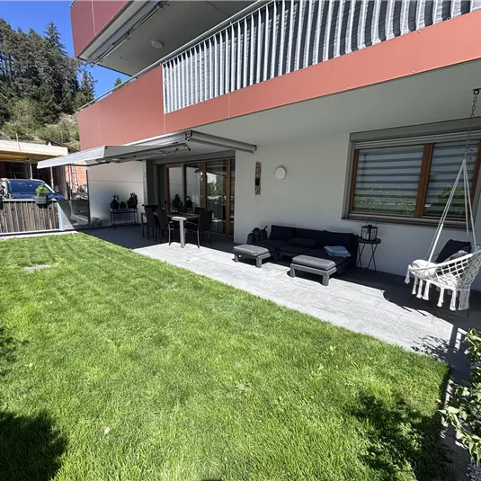 A modern terrace with a well-kept, green lawn. On the terrace are cozy furniture and a hammock.