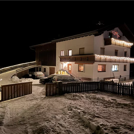 A bright, beautifully decorated winter evening with a lit house. The snow is thick, and the surroundings are quiet and festive.