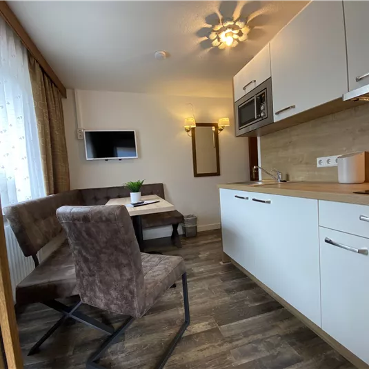 A modern kitchen with a dining area and a television. Plenty of light comes through the window, creating an inviting atmosphere.