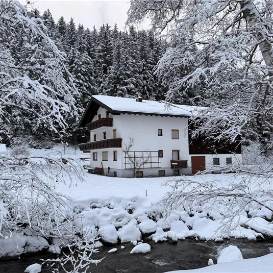 A cozy house in a snowy landscape. The garden and the river are surrounded by a thick blanket of snow.