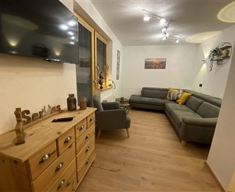 Ein modernes Wohnzimmer mit einer grauen Couch und einem Holztisch. Große Fenster bringen viel natürliches Licht in den Raum.