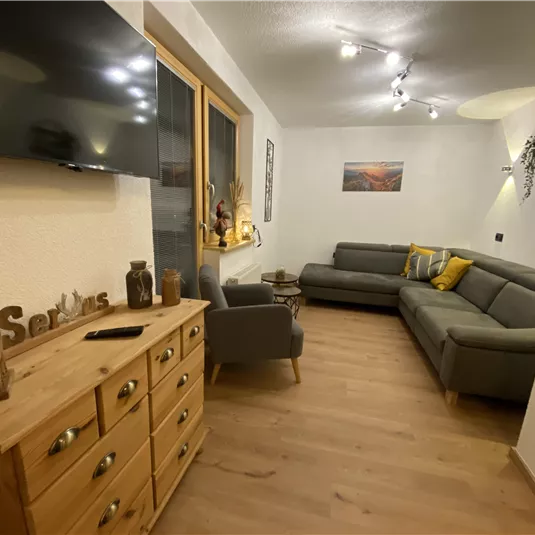 A modern living room with a gray sofa and a wooden table. Large windows bring a lot of natural light into the room.