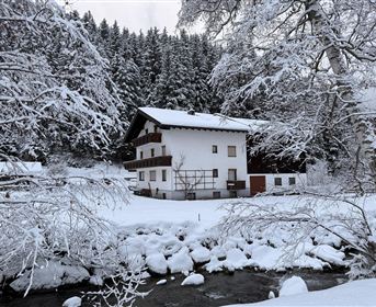 Ein gemütliches Haus in einer verschneiten Landschaft. Der Garten und der Fluss sind von einer dicken Schneedecke umgeben.