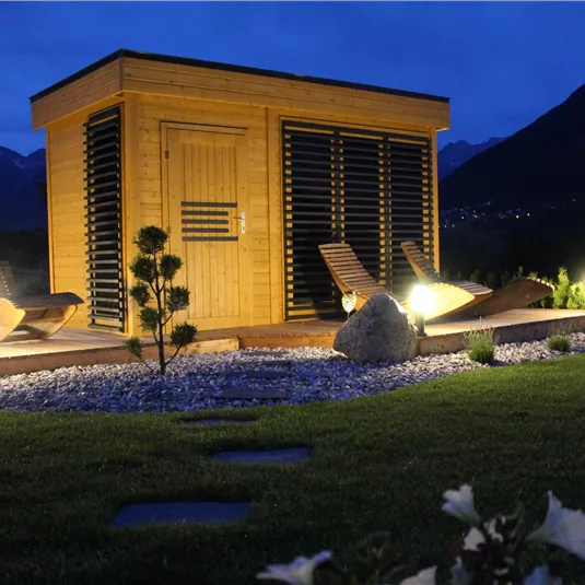 A modern sauna in a shaded outdoor area. The surroundings are beautifully designed with stones and green spaces.