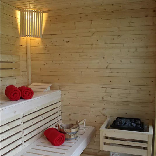 A modern sauna with bright wooden paneling and red towels. The relaxing atmosphere is complemented by soft lighting and a practical sauna control system.