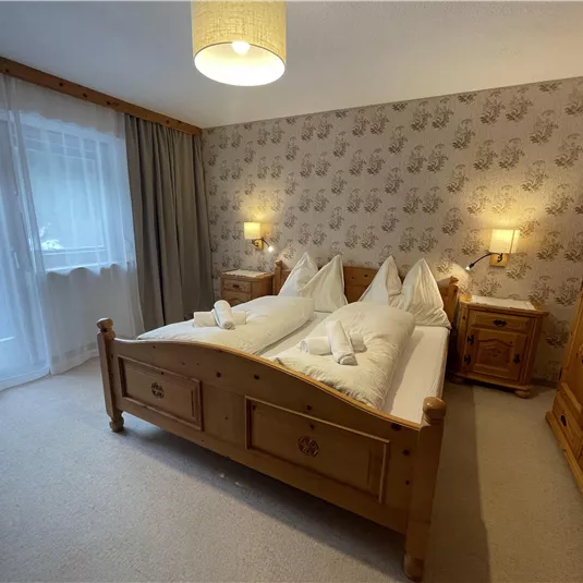 A cozy bedroom with a large wooden bed and two nightstands. The walls are decorated with a simple pattern and there is plenty of daylight through the window.