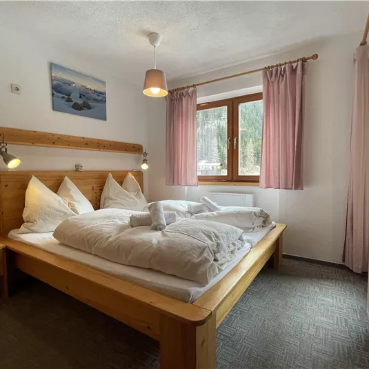A cozy bedroom with a double bed and wooden furniture. Large windows let in plenty of daylight and there is a beautiful view of nature.