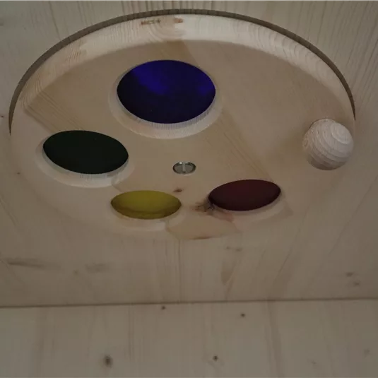 Eine hölzerne Spielzeugplatte mit vier farbigen Löchern und einer kleinen Holzkuppel. Eine Holzperle ist neben den Löchern positioniert.
