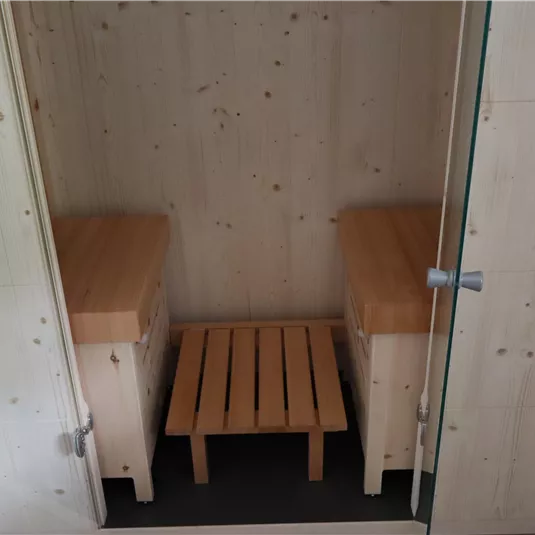 Ein moderner Saunabereich mit zwei Sitzbänken aus Holz. Die Wände sind schlicht und hell, was eine entspannende Atmosphäre schafft.