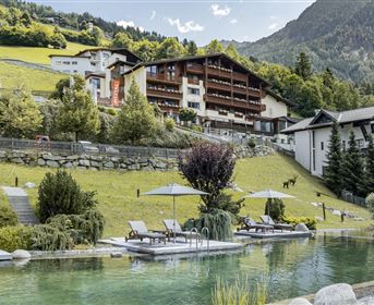 Ein malerischer Poolbereich mit Liegen, umgeben von gepflegten Gärten und Bergen im Hintergrund. Das Gelände strahlt Ruhe und Naturverbundenheit aus.
