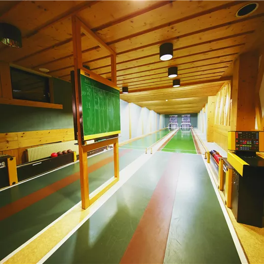 Eine geschlossene Kegelbahn mit Holzverkleidung und buntem Bodenbelag. Die Bahn ist gut beleuchtet und bietet Platz für mehrere Spieler.